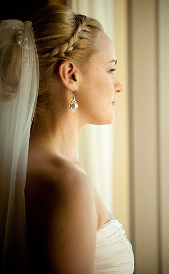Bride with a braided wedding hairstyle and veil looking at the window