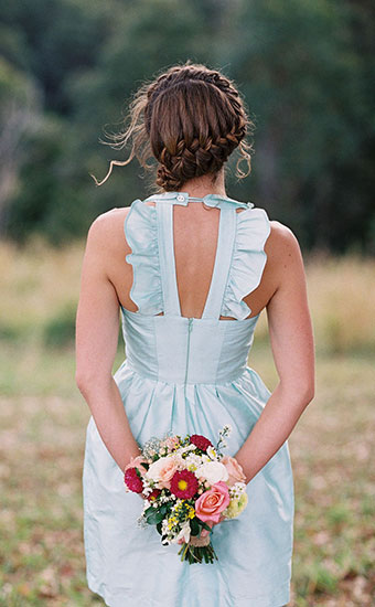 Back view of a bridesmaid in lightblue dress with a braid hairstyle holding a bouquet